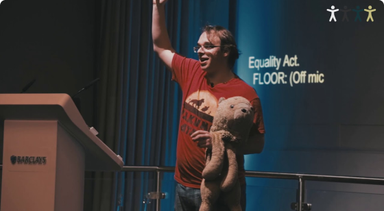 Jamie standing on stage raising right arm and holding stuffed lion with left arm